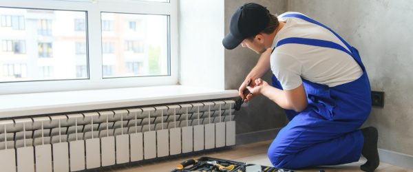 Cheerful male worker, plumber checking pipes while installing heating system in apartment.
